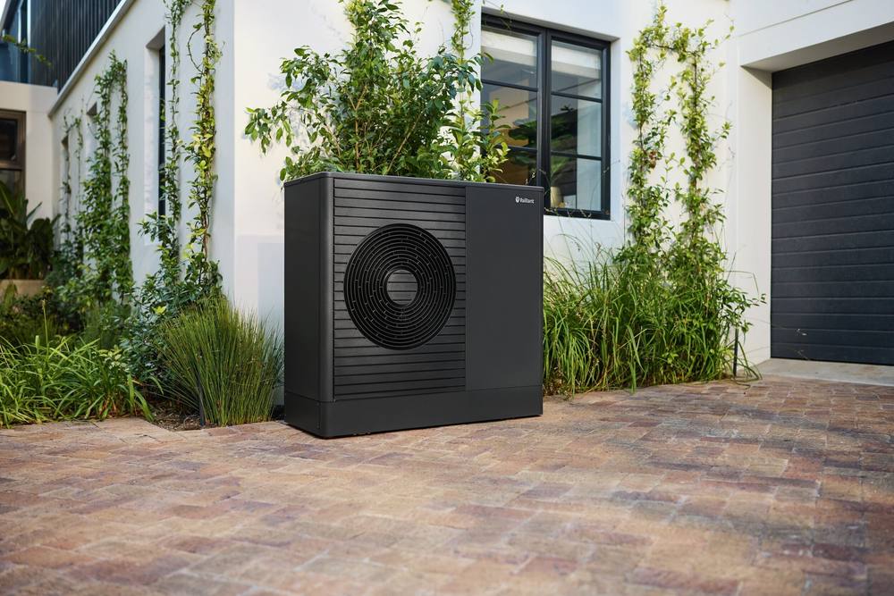 Vaillant aroTHERM plus tegen een witte gevel met klimplanten, op een klinkerbestrating