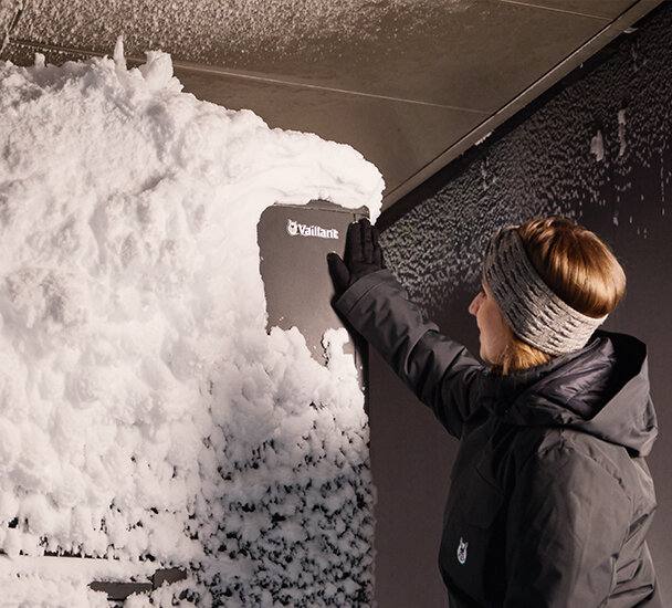 Vrouw veegt sneeuw van een Vaillant warmtepomp