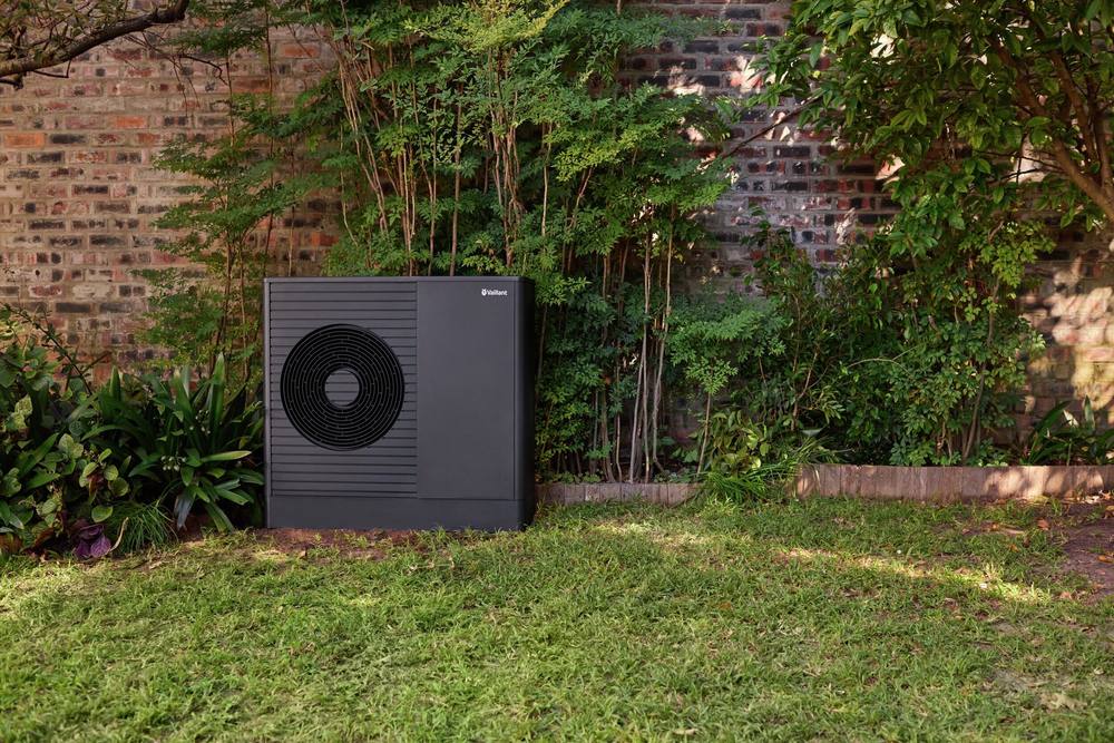 Vaillant warmtepomp tegen een bakstenen tuinmuur, tussen de beplanting